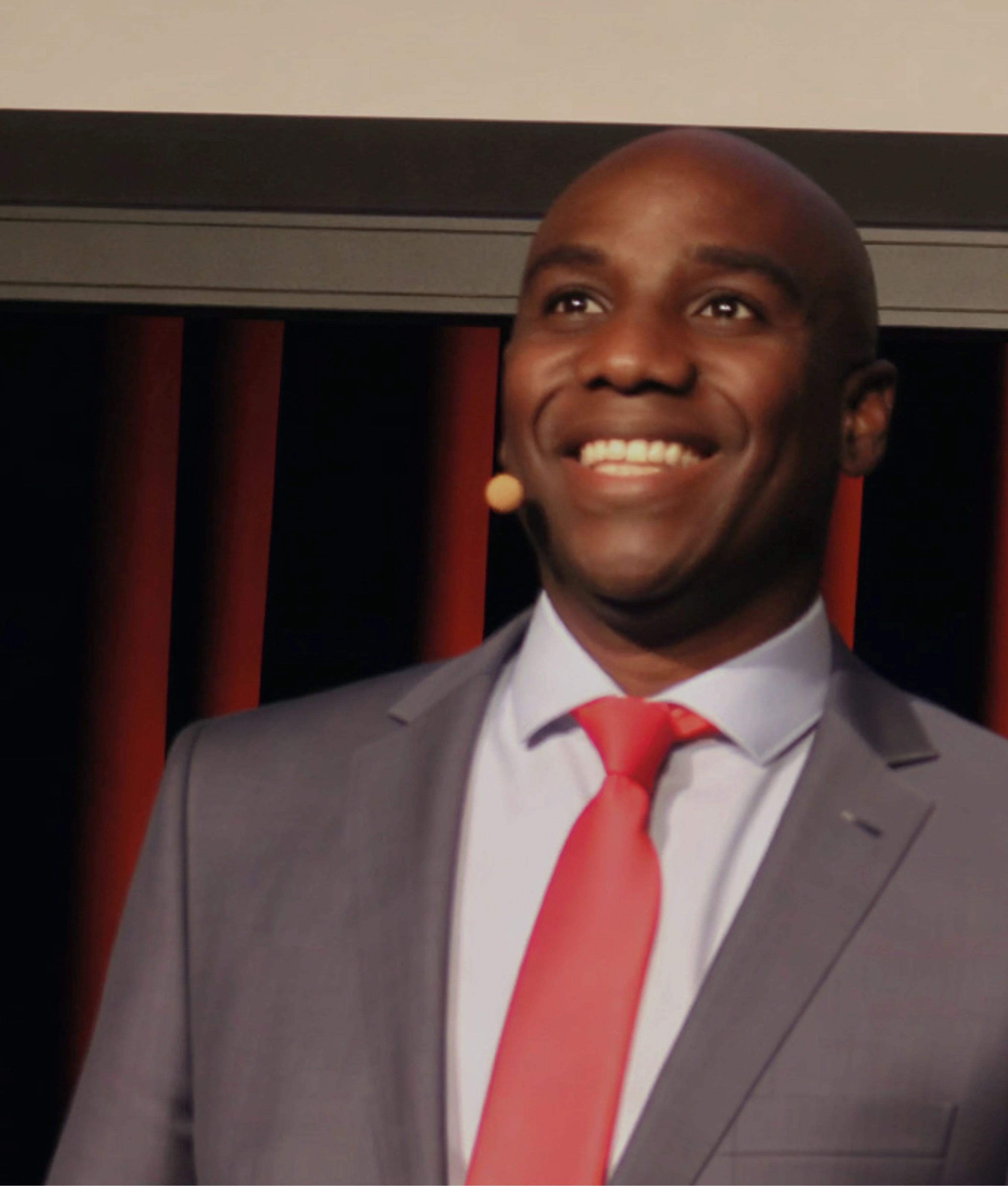 Foto van Otwien Vlieri op een witte achtergrond, lachend een arm leunend en de ander naast zijn lichaam.